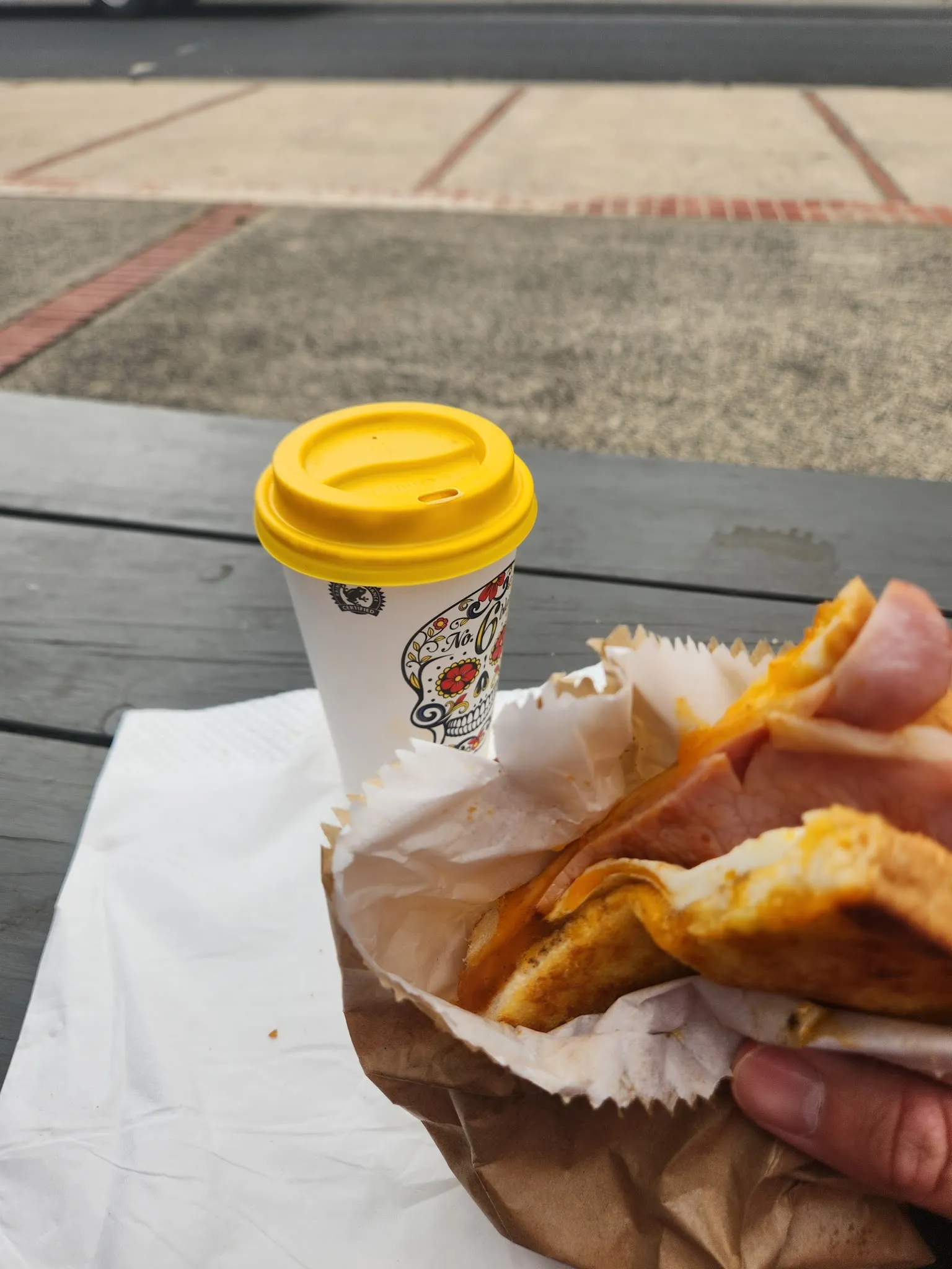 Egg and bacon toastie held in hand with a coffee: the classic breakfast deal