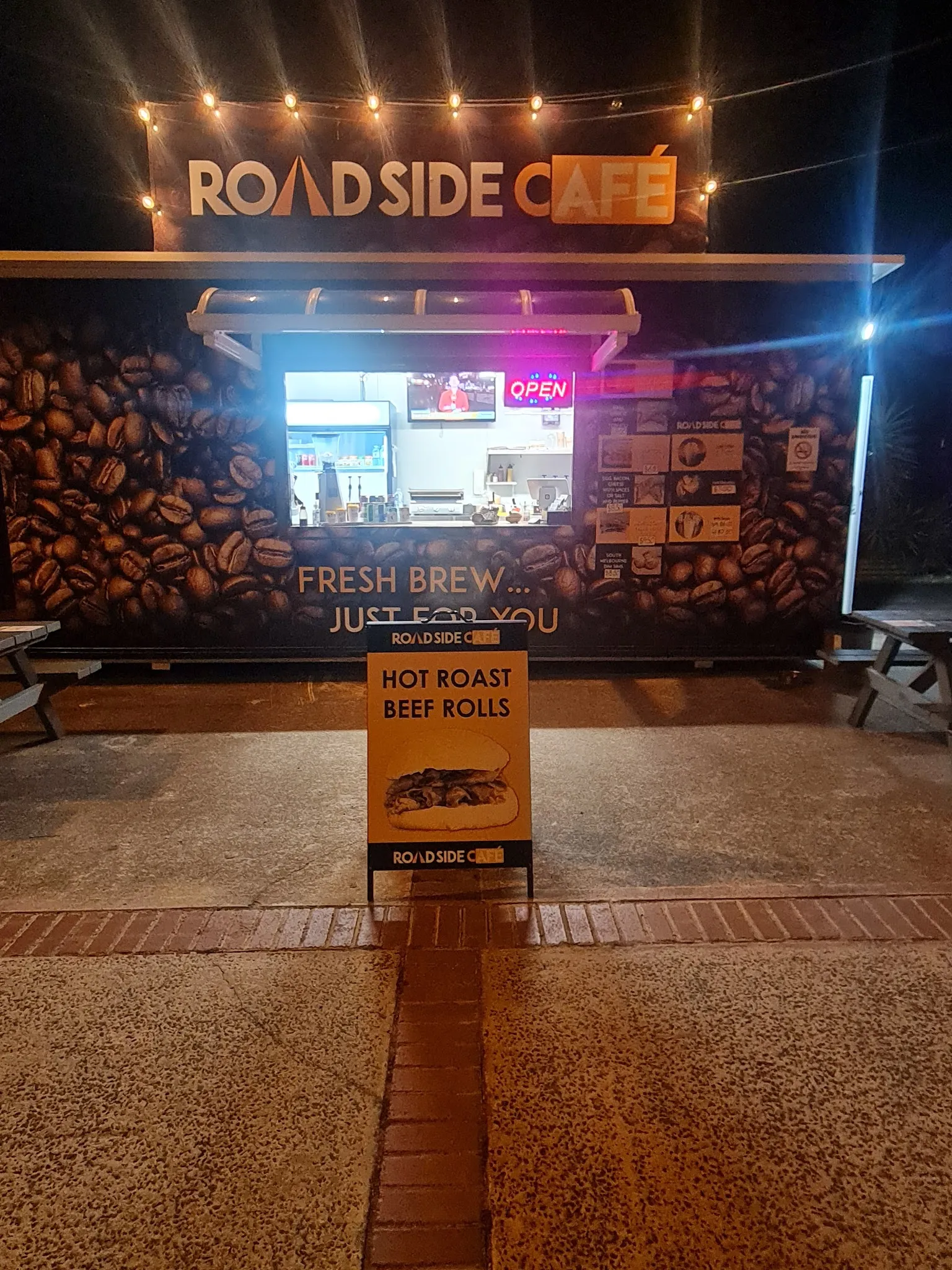 Roadside Cafe lit up at night with the Hot Roast Beef Rolls A-frame sign